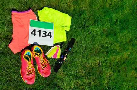 跑步鞋，马拉松比赛围兜 数，跑步者的齿轮和能量凝胶上草背景 体育 健身和健康的生活方式的概念