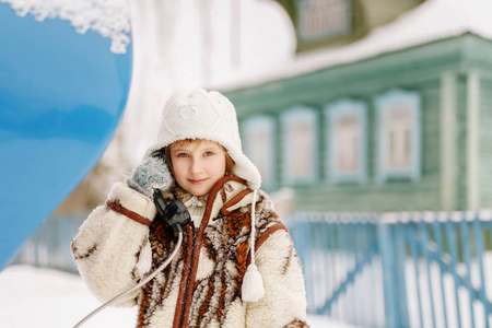 一件毛皮大衣 帽子和手套在冬天持旧手机手机和相机看年轻可爱的小女孩