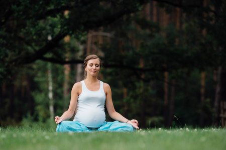 在荷花的立场上森林背景的孕妇瑜伽。在公园草地垫 户外 健康女人