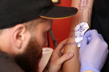纹身大师在工作室中将素描应用到男性手臂上，近距离观看