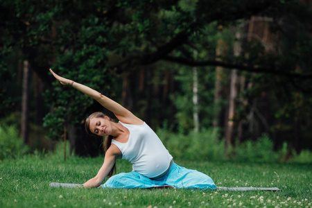 在荷花的立场上森林背景的孕妇瑜伽。在公园草地垫 户外 健康女人