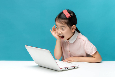惊讶 可爱的亚洲享受笔记本电脑在蓝色背景上的小女孩