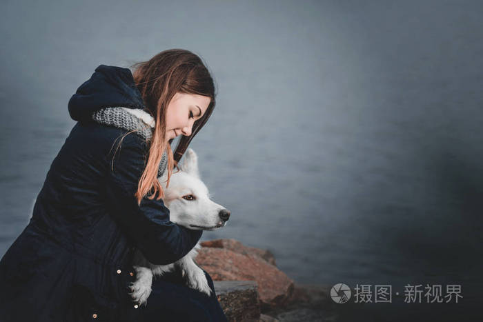 美丽少女拥抱她白色的狗在河岸边秋天的早晨