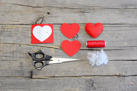如何把情人节缝毡的心。教程。红感到心，切感到件形状中的一颗心，合成填料，纸模板，剪刀，线，针木制的桌子上。顶视图