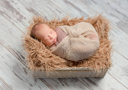 可爱熟睡的婴儿裹在毛茸茸的毯子的篮子