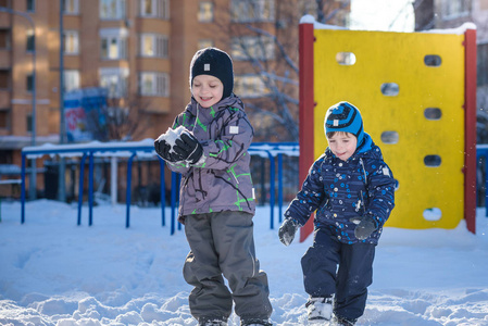 两个小家伙男孩在颜色鲜艳的衣服在降雪期间在户外玩。积极的休闲活动，与孩子在天冷的冬天。快乐的兄弟姐妹和双胞胎玩雪