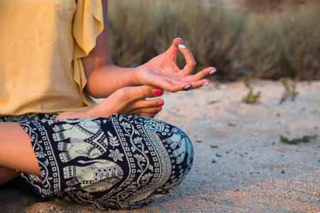 在日落时在海滩上一个瑜伽姿势打坐一个女人的手