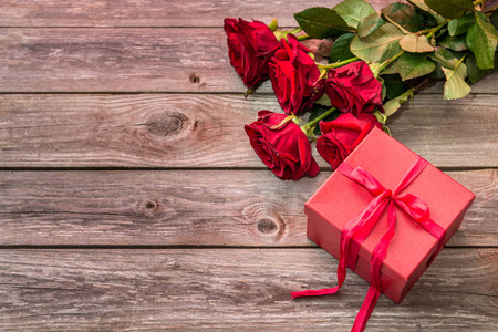 用弓和束红玫瑰木背景上的红色礼品盒。情人节背景