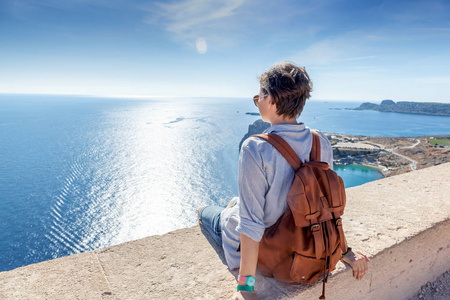 年轻女人旅行者坐在俯瞰着大海。旅行对格力