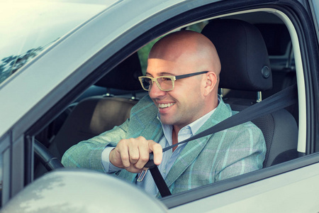 特写肖像英俊的男人快乐的微笑在他的车问显示你要系好安全带。安全之旅交通和车辆的概念