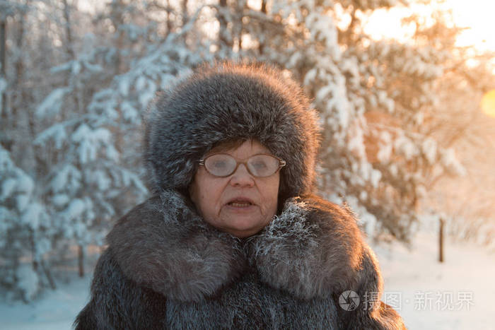 高级妇女毛皮外套和帽子的画像站立在寒冷的冬天雪覆盖的森林