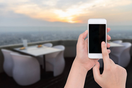 女手一直举着手机上模糊的晚餐桌上摆放了城市背景下的夕阳照片