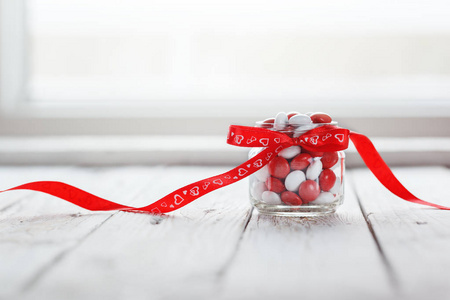 五颜六色的糖果罐装饰着白色的木制背景上的红色的弓心。情人节的概念