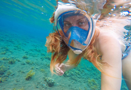 美丽的女人在水下游泳.红色头发女孩浮潜在蓝色面具照片