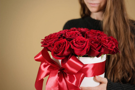 穿黑夹克抱着牵手丰富礼品花束 21 红玫瑰的女孩。在白色的帽盒花的组成。带着弓和宽红丝带绑