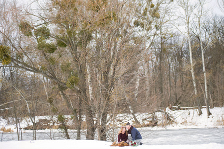 时尚美丽的年轻夫妇新娘和新郎，狗坐在冬季景观河道的背景