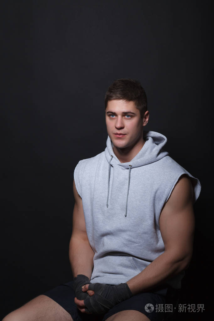 年轻的肌肉拳击手坐在黑色背景上的椅子上