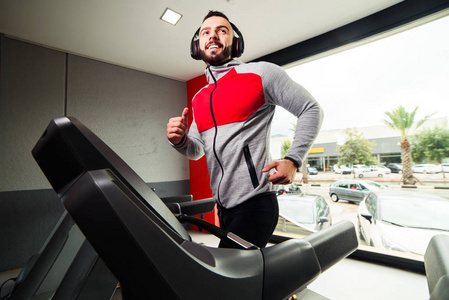 带着耳机在健身房的跑步机上锻炼的男人微笑着