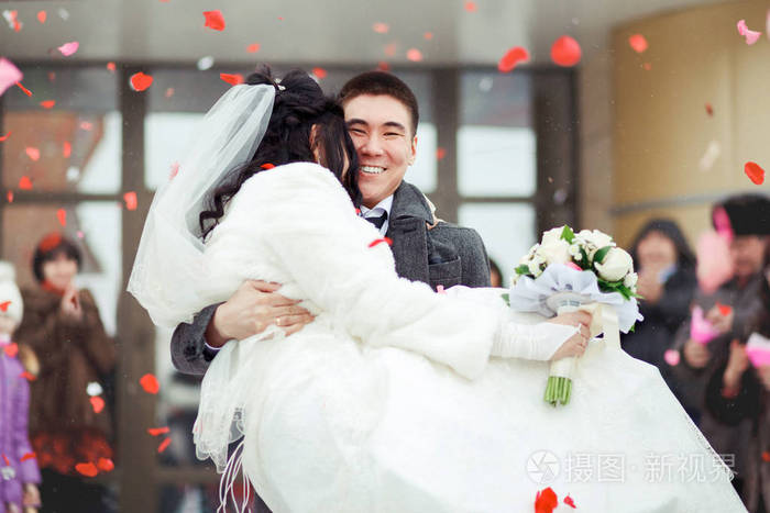 他抱新娘新郎,人群抛出花瓣和大米.新婚快乐