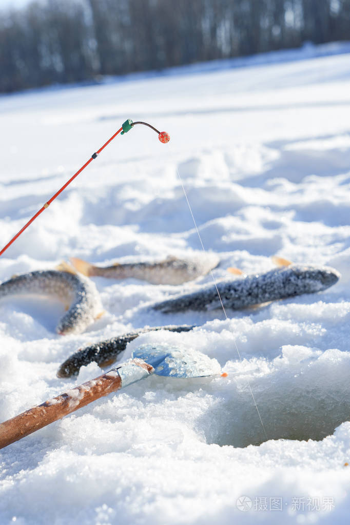 冬季捕鱼时靠近洞口的冰上的鱼和鱼竿
