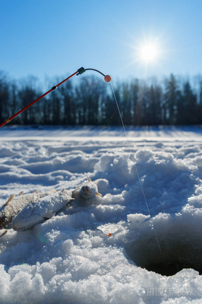 冬季捕鱼时靠近洞口的冰上的鱼和鱼竿