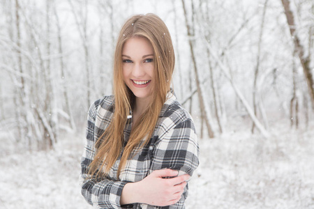 年轻的女子站在雪与波西米亚帽子和毯子附近树木