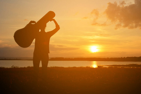 快乐的女人和吉他天空日落时的剪影照片