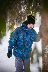 男人在冬天的公园里散步。幽默和微笑的家伙，温暖的衣服走在户外，看着针叶树