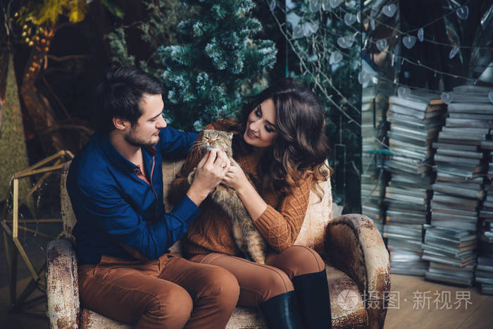 美丽热恋中的情侣和一只猫在他们的怀里坐在沙发上,拥抱,微笑和亲吻.