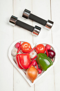 运动和饮食。健康的生活方式。蔬菜 哑铃。辣椒 西红柿 大蒜 洋葱萝卜在白色背景上的一颗心