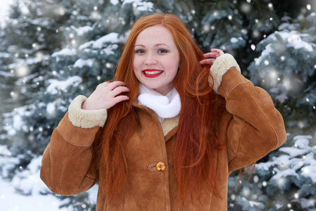 美丽的女人，在冬季户外 雪杉树在森林里，长长的红色头发，穿着一件羊皮大衣