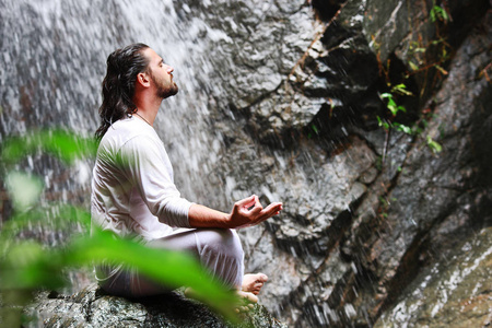 男人坐在石头上的冥想瑜伽在热带的瀑布