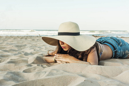 女孩躺在海滩穿沙滩夏天帽和短牛仔裤
