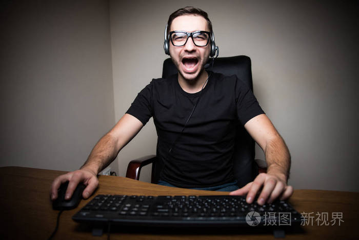 尖叫声年轻人戴着耳机玩电脑游戏