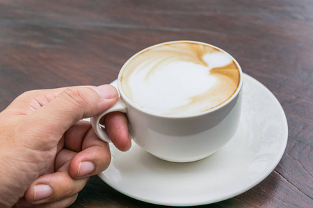 男子手持杯热咖啡与更多的奶泡在玻璃桌上。爱咖啡概念