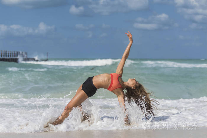 女孩在瑜伽姿势，她的腿上海滩上的海浪