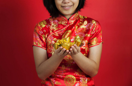 亚洲女人与旗袍持有黄金锭红色背景上