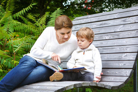 小男孩和他妈妈坐在公园的长椅上读b