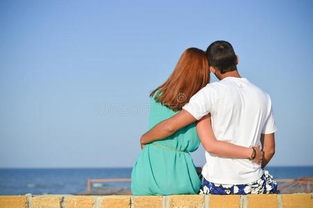 一对浪漫幸福的夫妇坐在沙滩上拥抱大海