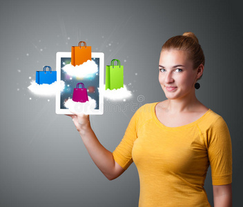 手持现代平板电脑的女人在云端挂着五颜六色的购物袋