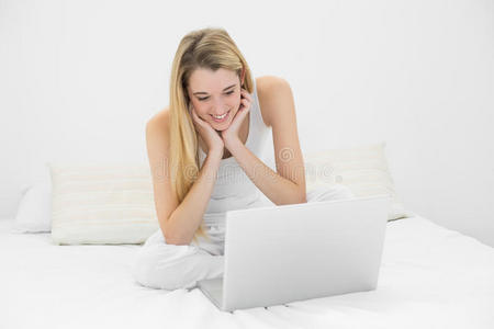 坐在床上用笔记本电脑工作的快乐的年轻女子