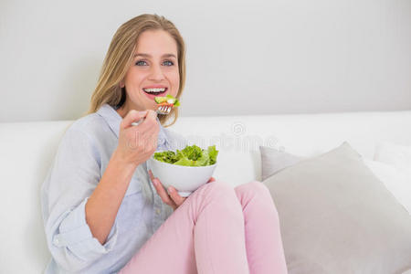 微笑的金发女郎坐在沙发上吃沙拉