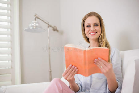 微笑的金发女郎坐在沙发上拿着一本书