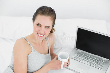 床上放着笔记本电脑和咖啡杯的一位微笑的休闲女士的肖像