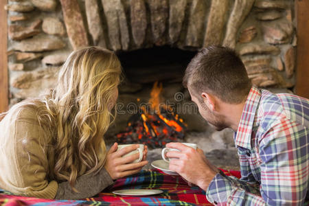 一对悠闲的夫妇拿着茶杯看着点燃的壁炉