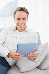 沙发上使用数码平板电脑的休闲微笑男士肖像