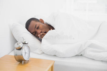 非洲男人在床上打哈欠，闹钟在前面
