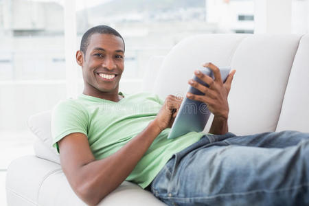沙发上用数字平板电脑随意微笑的非洲男人