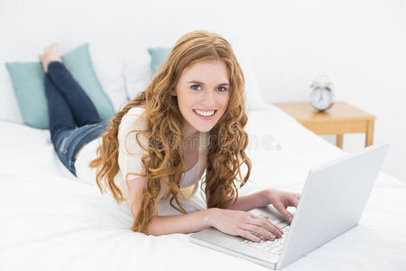 在床上用笔记本电脑微笑的金发女郎