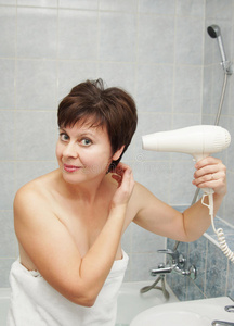 漂亮的中年妇女在浴室里吹干头发